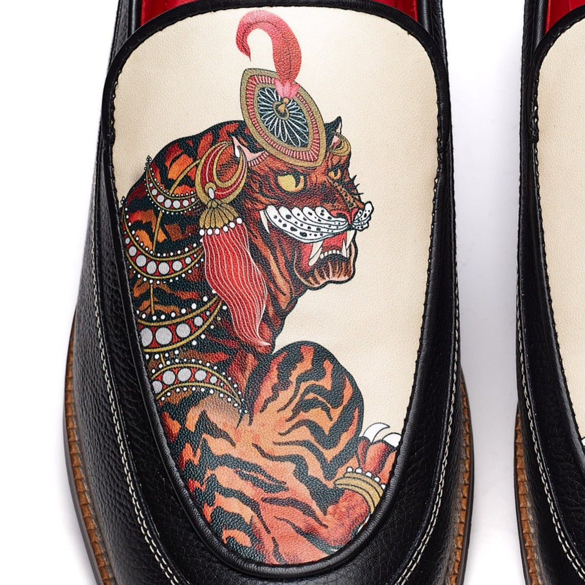 Black loafer with a detailed tiger/lion design on the insole against a white background